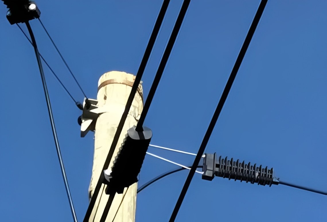 A PA1500 Dead-End Clamp securing an insulated aerial cable to a wooden utility pole against a clear blue sky