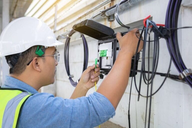 A technician in a hard hat and safety vest installs Fiber Optic Enclosures on a wall