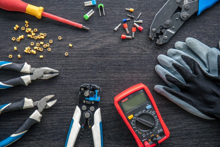 Various Electric Cable Tools, including crimpers, wire strippers, pliers, a screwdriver, and a multimeter, on a dark wooden surface.
