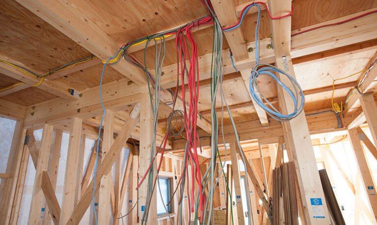 a variety of Electrical Building Wire cables hanging from the ceiling and running through the wooden frame of a building under construction