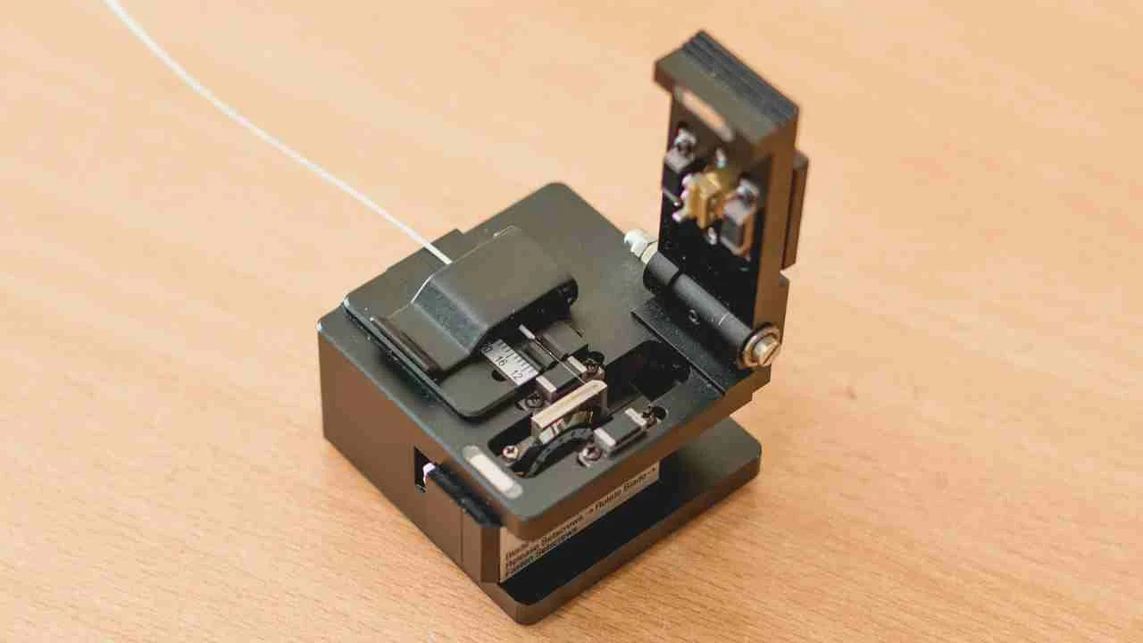 A professional-grade, black Optical Fiber Cleaver with a fiber optic cable secured in its V-groove, ready for the high-precision scribing and breaking process