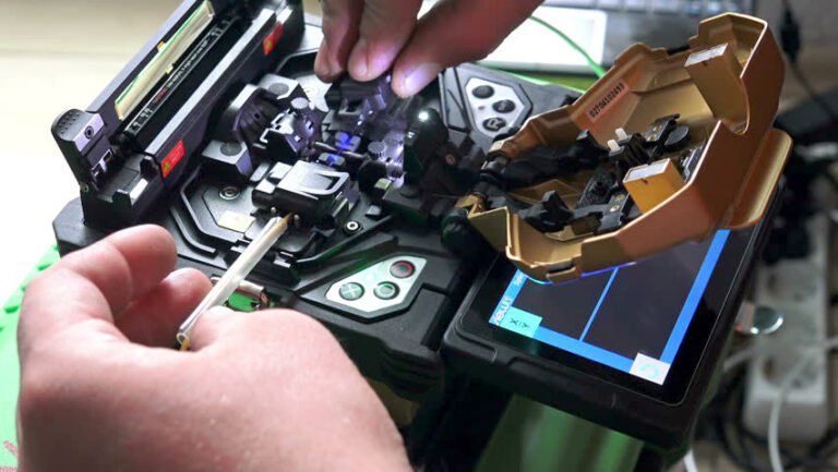 hands operating a Fiber Optic Fusion Splicer, preparing to splice fiber optic cables